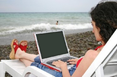 girl sitting on a beach with laptop